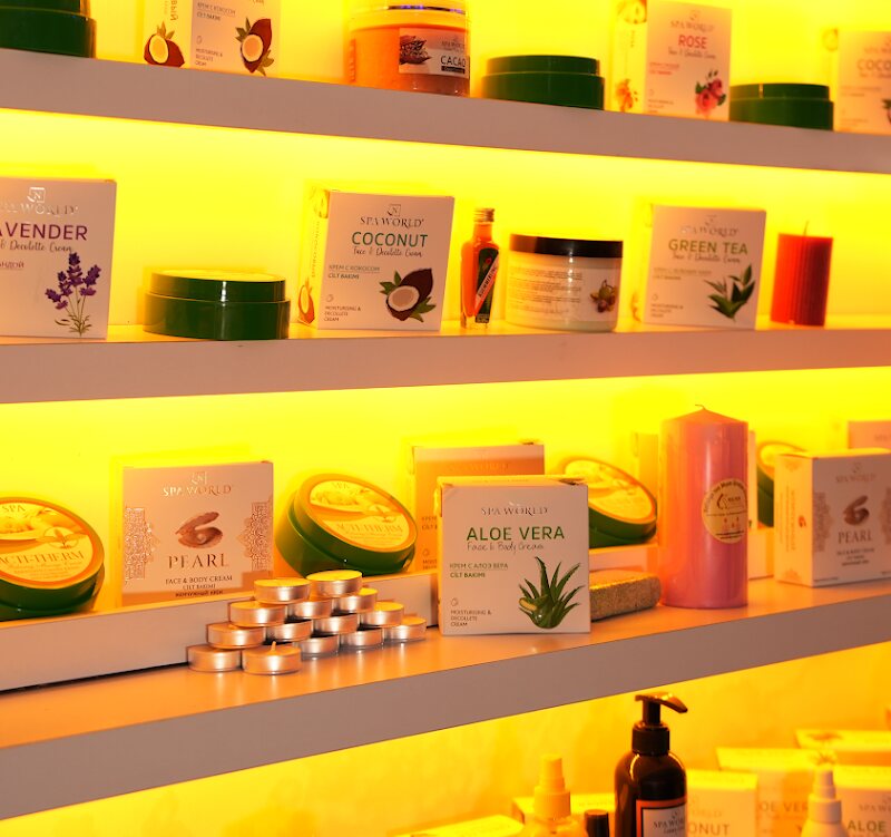 Backlit shelf of scrub and cream jars — lavender, coconut, green tea, aloe vera, rose.