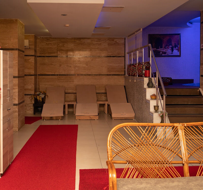 Row of loungers against a travertine wall, with a red runner and a wicker seat by the stairs.
