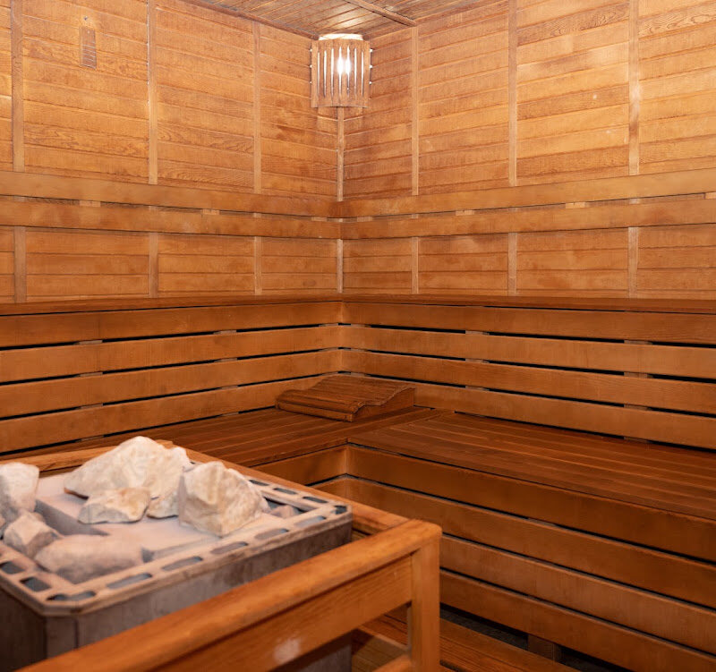 Wooden sauna with tiered benches and a stone heater in the corner.